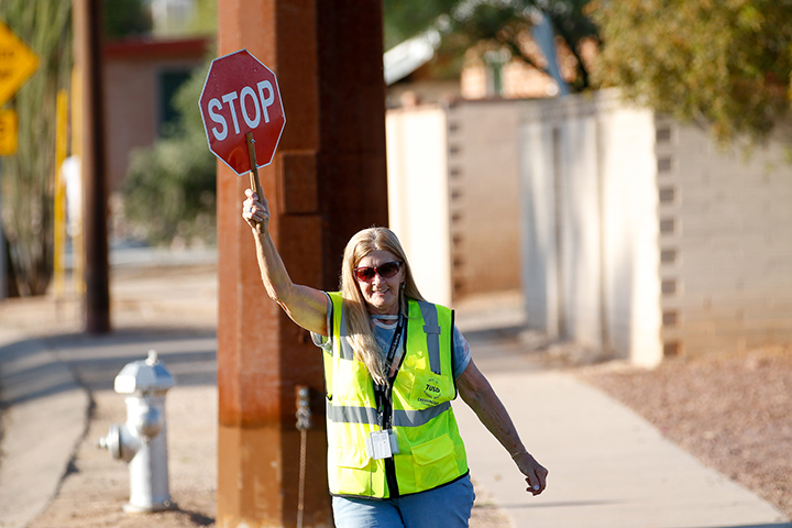A woman in a yellow safety vest holds up a stop sign in the crosswalk