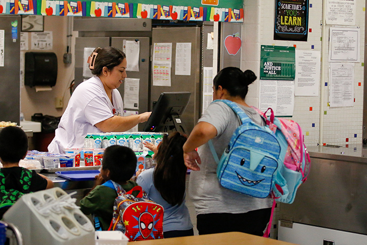 A woman rings up a mom and her kids at the cash register in the cafeteria