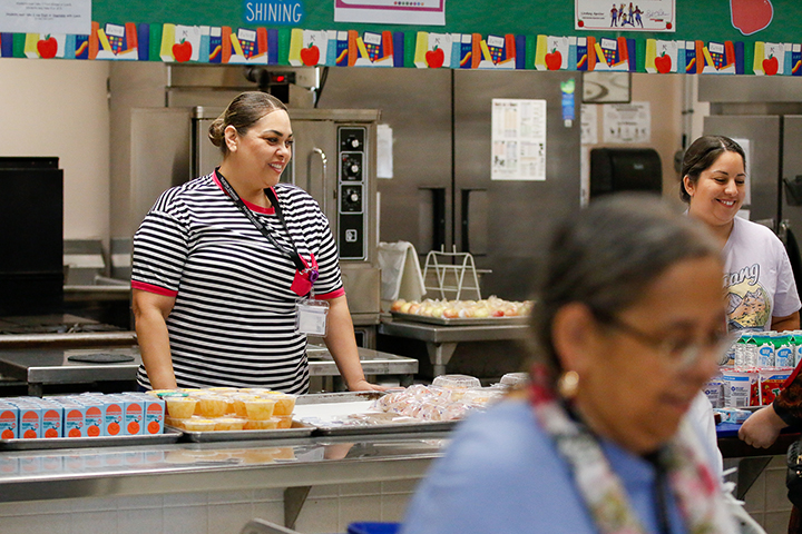 A woman in a striped shirt smiles behind the counter in the cafeteria