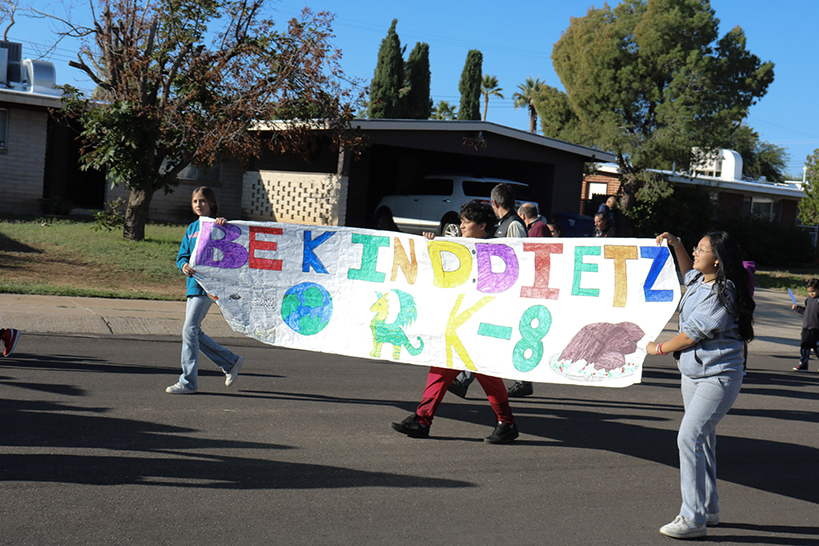 Students march while holding a hand-drawn banner with the words Be Kind Dietz K-8