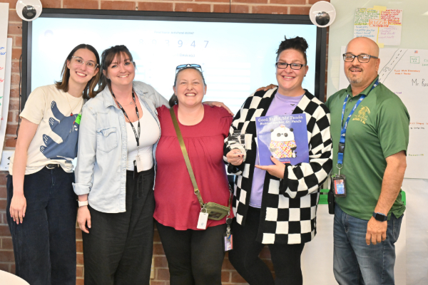 A woman in a black and white jacket, second from right, holds up her award and a book with her fellow staff members